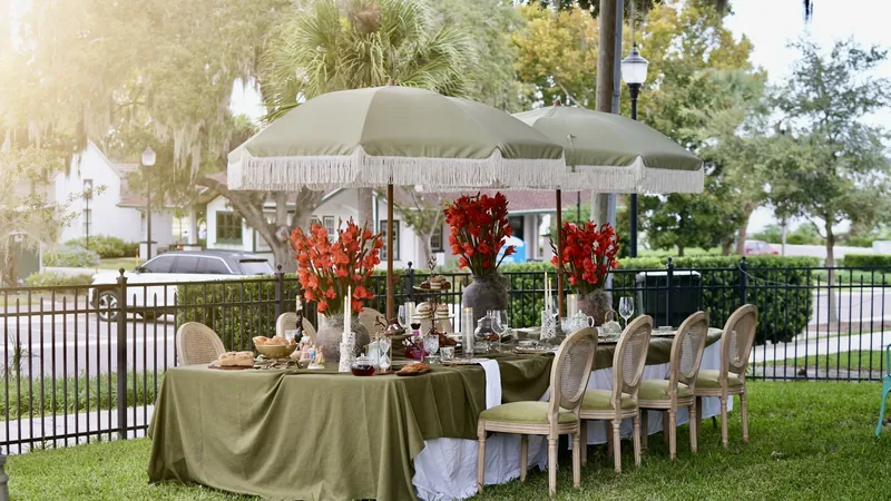 An outdoor tea table with sage linens, flowers and fringed umbrellas.