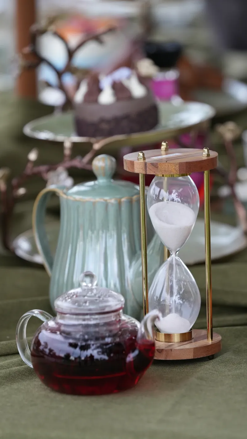 A glass teapot and hourglass on a garden tea table.